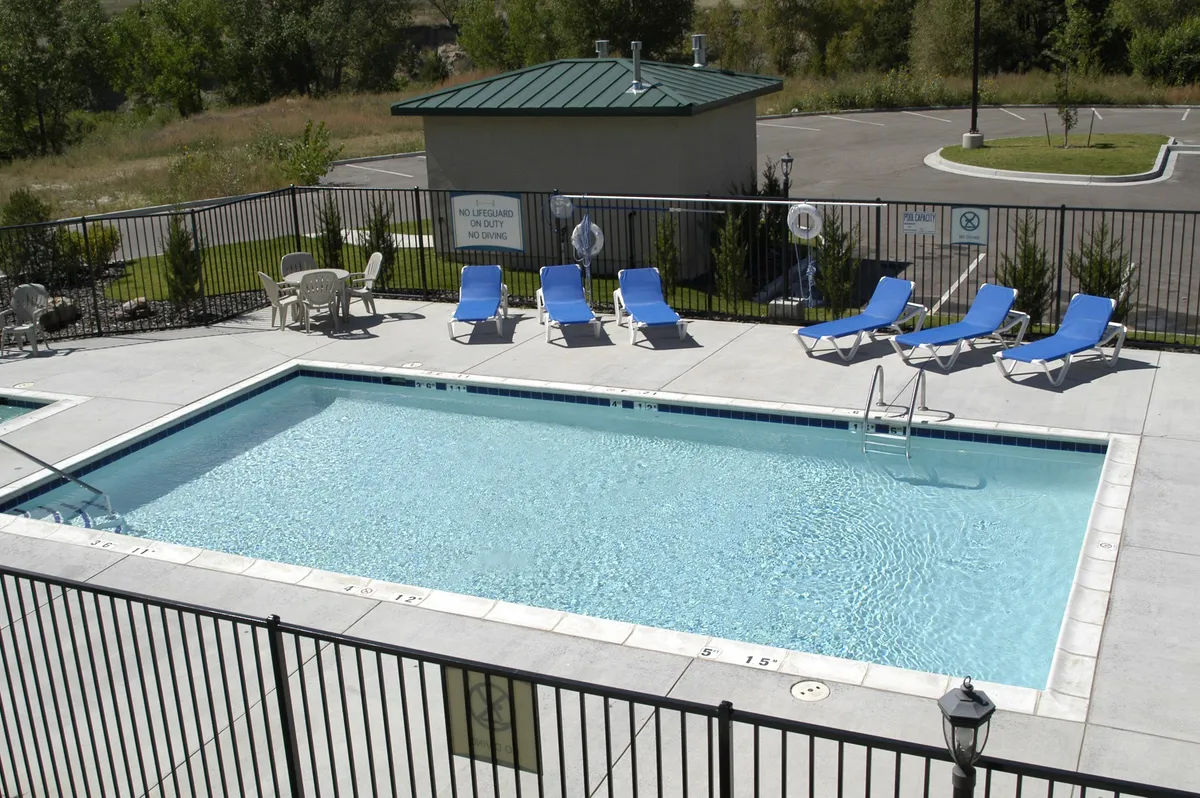 A sunlit swimming pool area is surrounded by lounge chairs, a lifeguard station, and lush greenery, conveying a relaxed, resort-like setting. The pool is ready for both active play and quiet relaxation, while nearby amenities provide added convenience for guests.