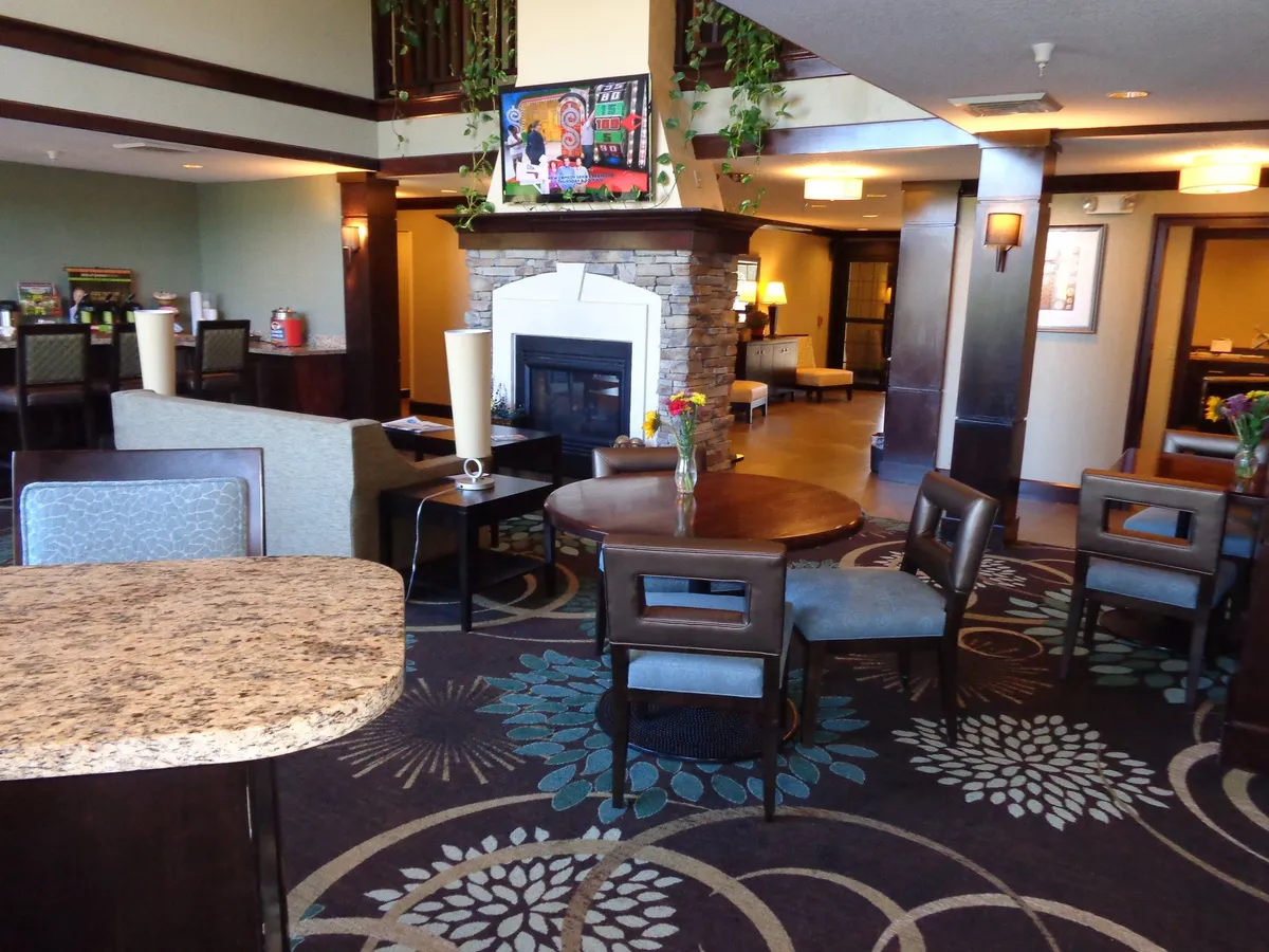 A warm, inviting living room with a fireplace as the focal point, surrounded by a round dining table, comfortable seating, and tasteful decorative artwork. The arrangement suggests a space perfect for unwinding with family or friends, socializing, or enjoying quiet evenings in. The overall mood is one of comfort and homelike charm.