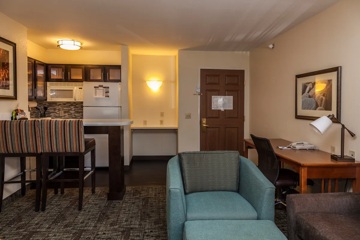 The image showcases a comfortable, well-lit interior featuring a modern kitchenette, a cozy seating area, a functional desk for work or planning adventures, and the entrance door. The space feels warm and inviting, designed for both relaxation and productivity.