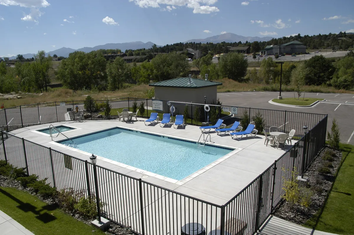The image showcases the resort's inviting outdoor heated swimming pool, surrounded by comfortable lounge chairs and enclosed by a tasteful poolside fence. Lush greenery frames the area, providing a peaceful backdrop for relaxation. The setting hints at leisurely afternoons, friendly gatherings, or quiet moments by the water, all beneath the open Colorado sky.