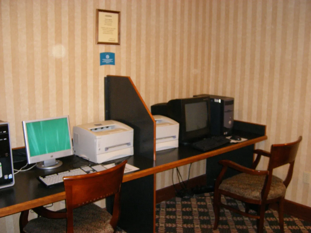 A functional business center interior equipped with computers, printers, and comfortable chairs, providing a dedicated workspace for productivity. The environment is quiet and organized, ideal for individual work or small meetings.